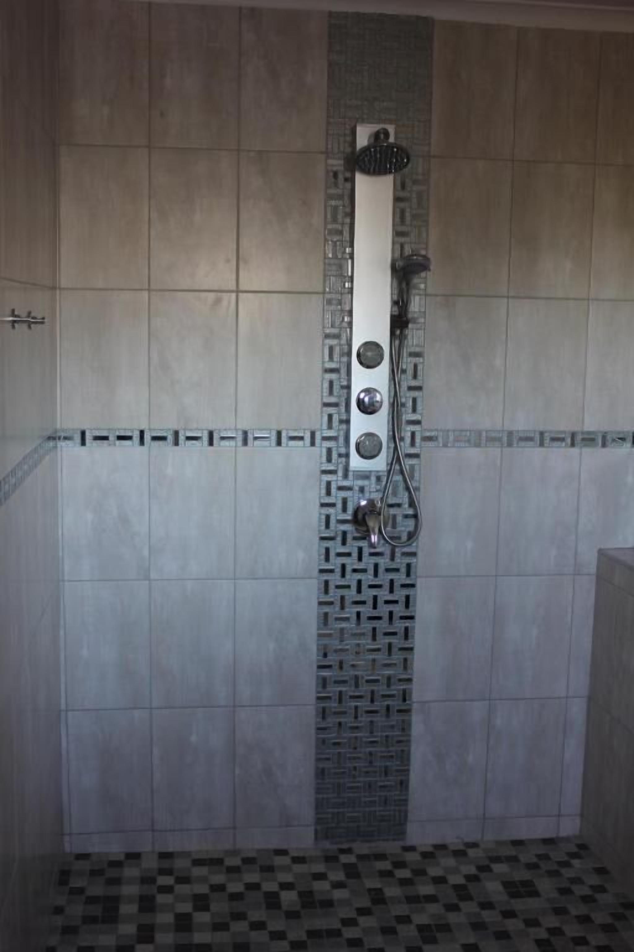 Un baño con ducha, paredes de azulejos y piso estampado.