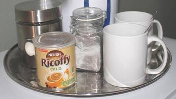 Una bandeja con un bote de café molido Nescafe Ricoffy, un tarro de vidrio, una taza blanca y una tetera eléctrica blanca.