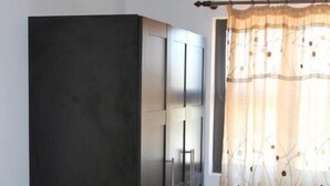 A room with a white sofa, a dark cabinet, and a window with a patterned curtain. - Coco Palm B&B (Windhoek)