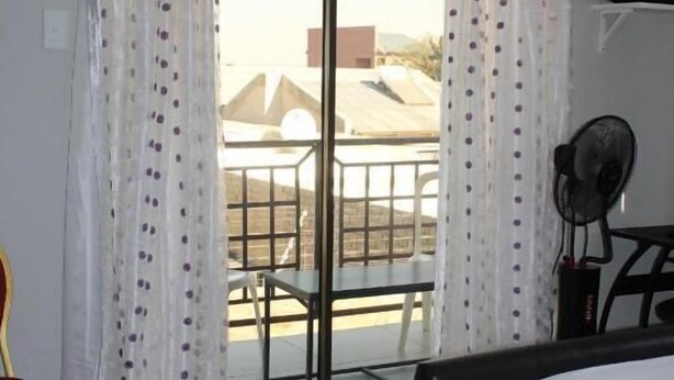 A hotel room with a bed, a chair, a table, and a balcony with a view. - Coco Palm B&B (Windhoek)