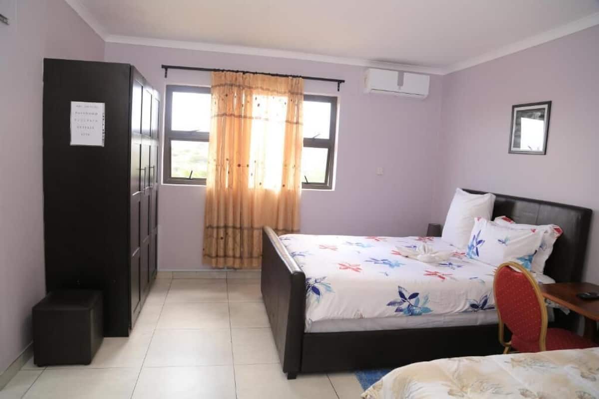Quarto com cama, guarda-roupa, janela com cortinas e uma pequena mesa.
