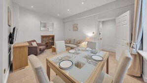 Un salon moderne avec un coin repas, comprenant un canapé, des fauteuils et une table à manger en verre, le tout disposé pour accueillir quatre personnes.