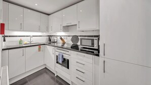 Une cuisine moderne avec des meubles blancs, un plan de travail noir, un four à micro-ondes, un grille-pain et un évier.