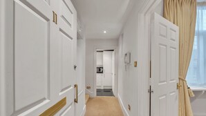 Un couloir avec des portes blanches, une moquette beige et une fenêtre ornée de rideaux beiges.