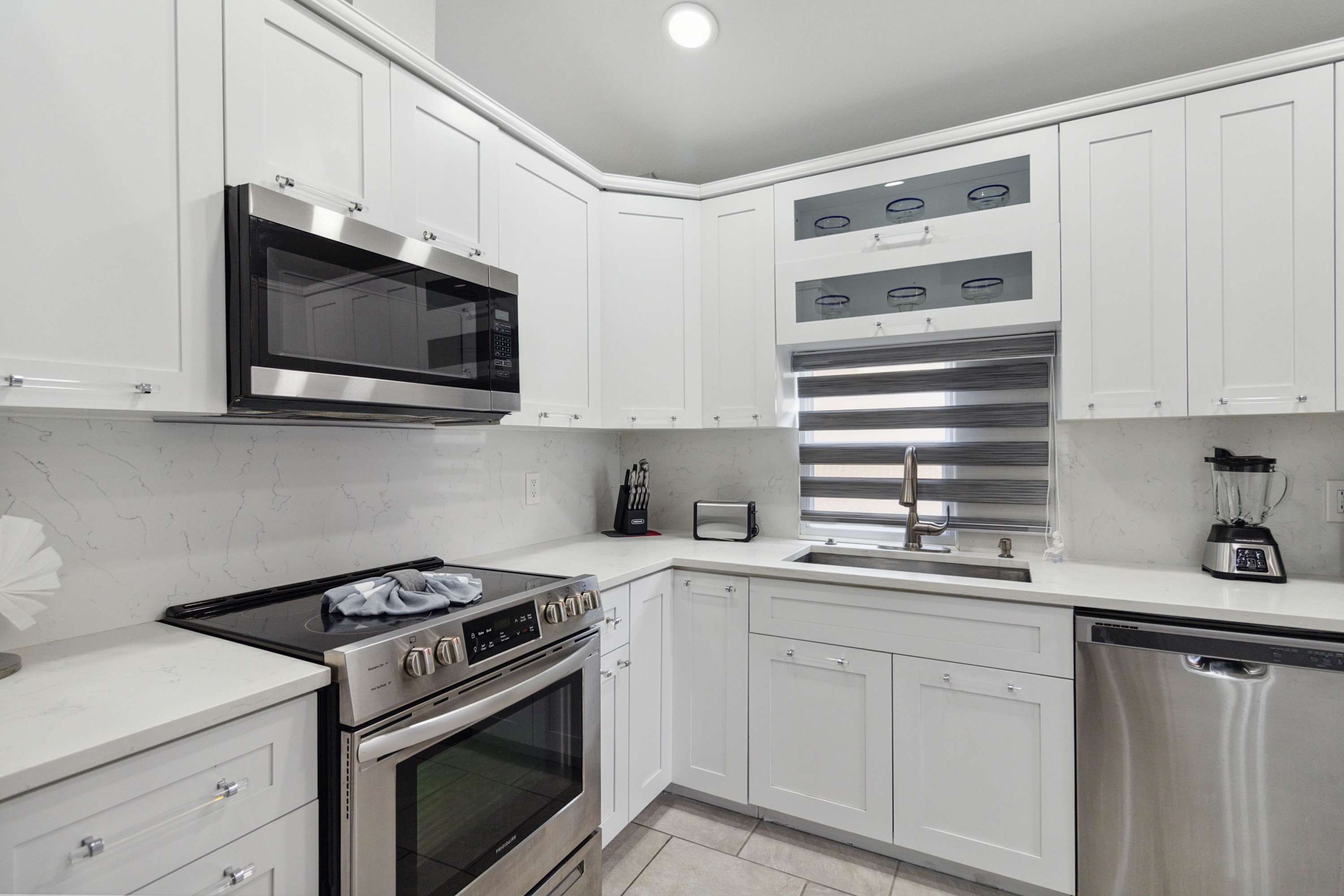A modern kitchen with white cabinets, a built-in microwave, a stainless steel oven, a toaster, and a dishwasher.