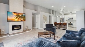 Ein modernes Wohnzimmer mit Kamin, einem großen Fernseher und einer Essecke mit Barhocker.