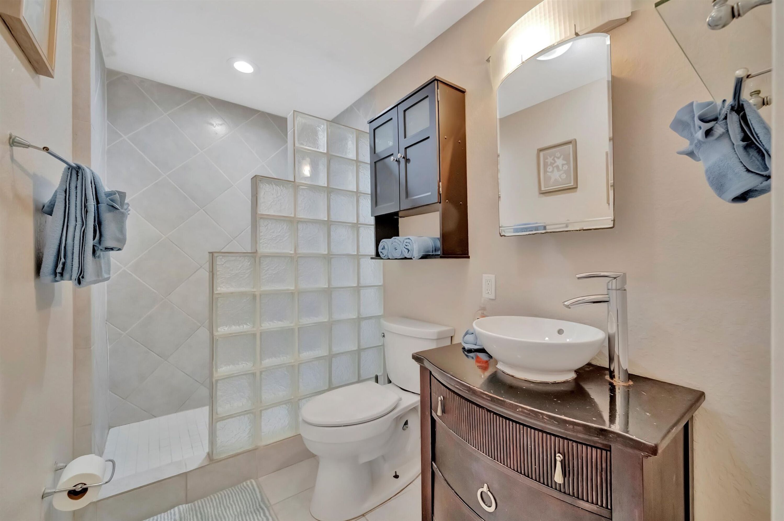Un baño con inodoro, lavamanos, mueble y zona de ducha con puertas de vidrio esmerilado.