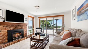 Ein Wohnzimmer mit Kamin, einer Couch, einem Fernseher und Blick ins Freie.