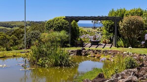 Ein Garten mit Teich, einer Pergola und einem Rasenwagen voller Pflanzen.