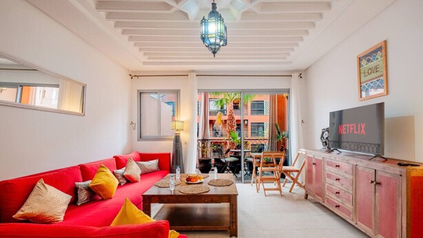 A living room with a red sofa, a coffee table, and a TV displaying 'NETFLIX'. - Cosy 1BR près Carré Eden – Terrasse & Confort (Marrakesh)