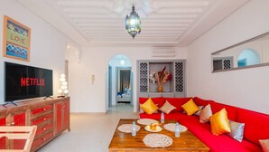 A living room with a red sofa, wooden coffee table, and a TV displaying 'NETFLIX'. - Cosy 1BR près Carré Eden – Terrasse & Confort (Marrakesh)