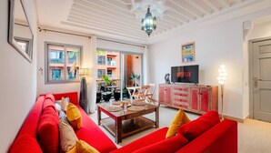 A living room with a red sofa, a wooden coffee table, and a TV on a cabinet. - Cosy 1BR près Carré Eden – Terrasse & Confort (Marrakesh)
