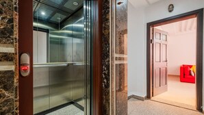 An elevator with a marble wall, a red button, and a red couch in the adjacent room. - Cosy 1BR près Carré Eden – Terrasse & Confort (Marrakesh)