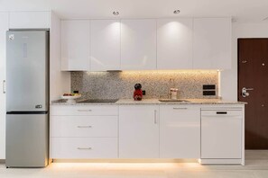 A modern kitchen with white cabinets, a granite countertop, a stainless steel refrigerator, and a dishwasher. - Orquideas Apparatus (Estepona)