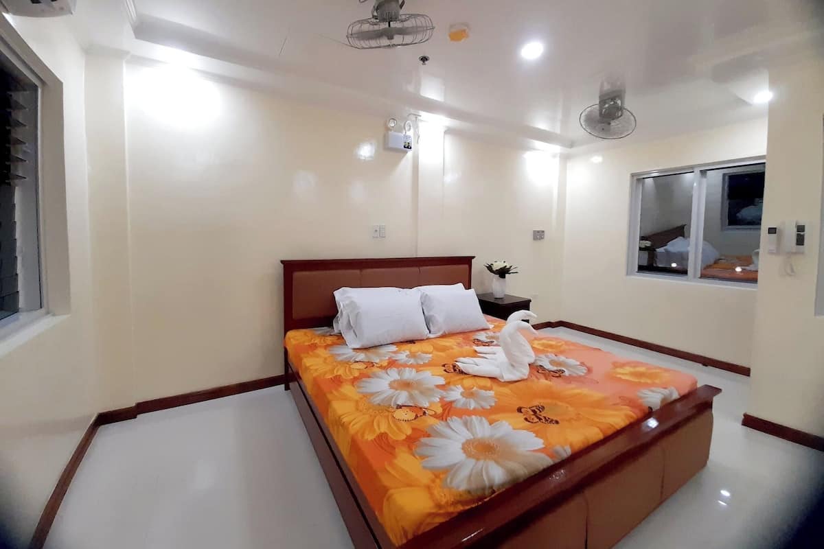 A hotel room with a bed, a bedside table, a nightstand, a window, and a ceiling fan.