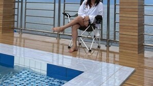 Una persona sentada en una silla de terraza junto a una piscina con vista al mar.
