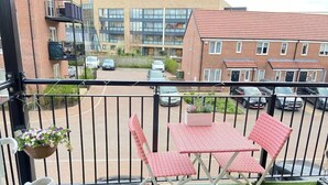 Un balcon avec une petite table et des chaises, une plante en pot et une sculpture blanche.