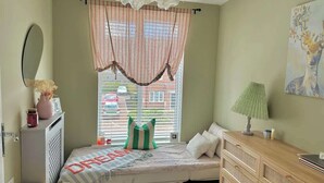 Une chambre confortable avec un lit, une commode, une fenêtre avec des rideaux, une lampe et un tableau au mur.