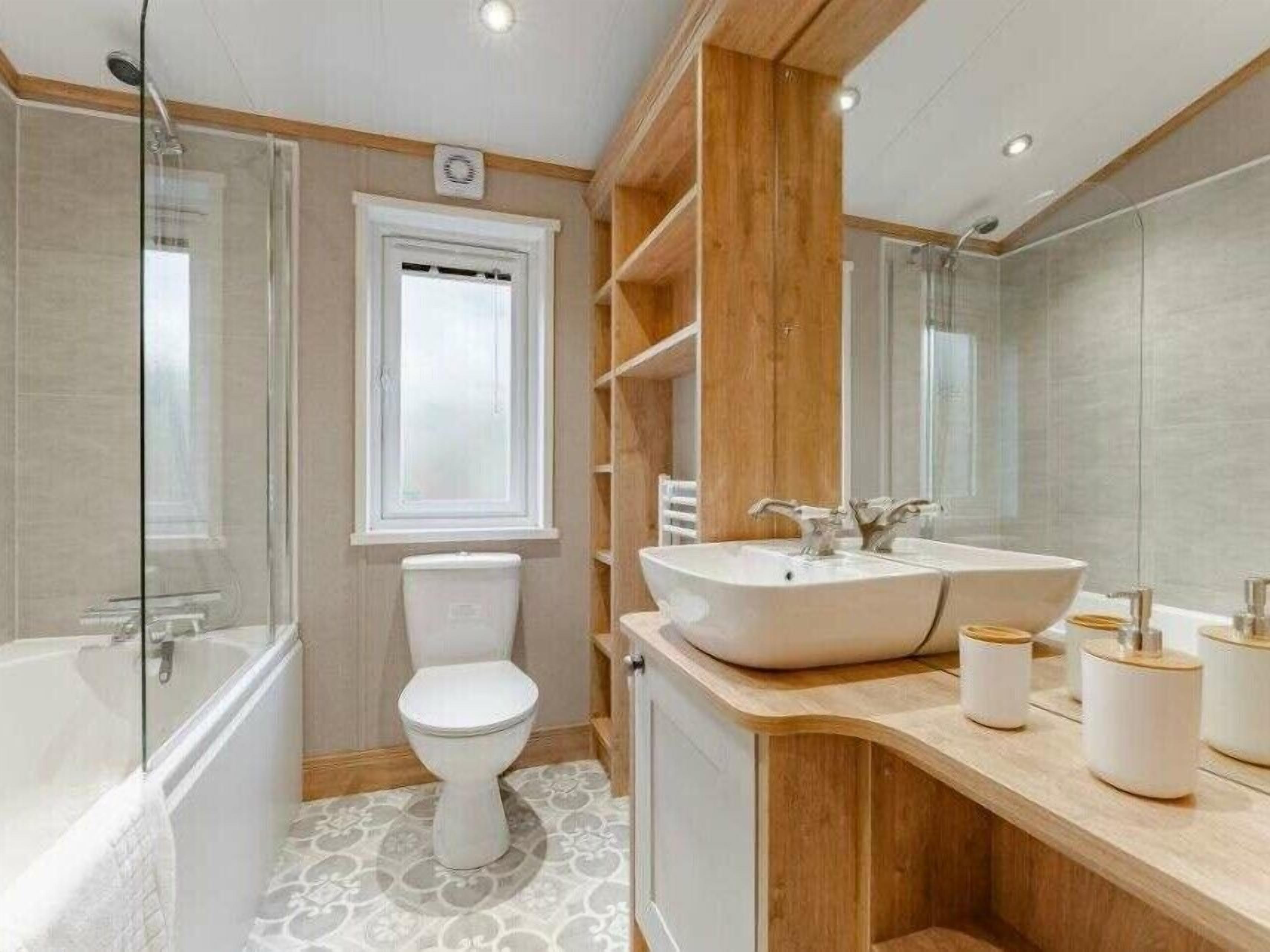 Une salle de bain moderne dotée d’une douche à parois de verre, de toilettes, d’un lavabo avec un miroir et de meubles en bois.