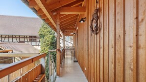 Een houten balkon met een leuning, een lamp en uitzicht op een gebouw met een pannendak.