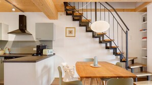 Een moderne keuken met een centraal eiland, een zithoek met een houten tafel en een wenteltrap.