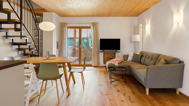 Een moderne woonkamer met houten plafond, een trap, een eethoek, een bank en een televisie.