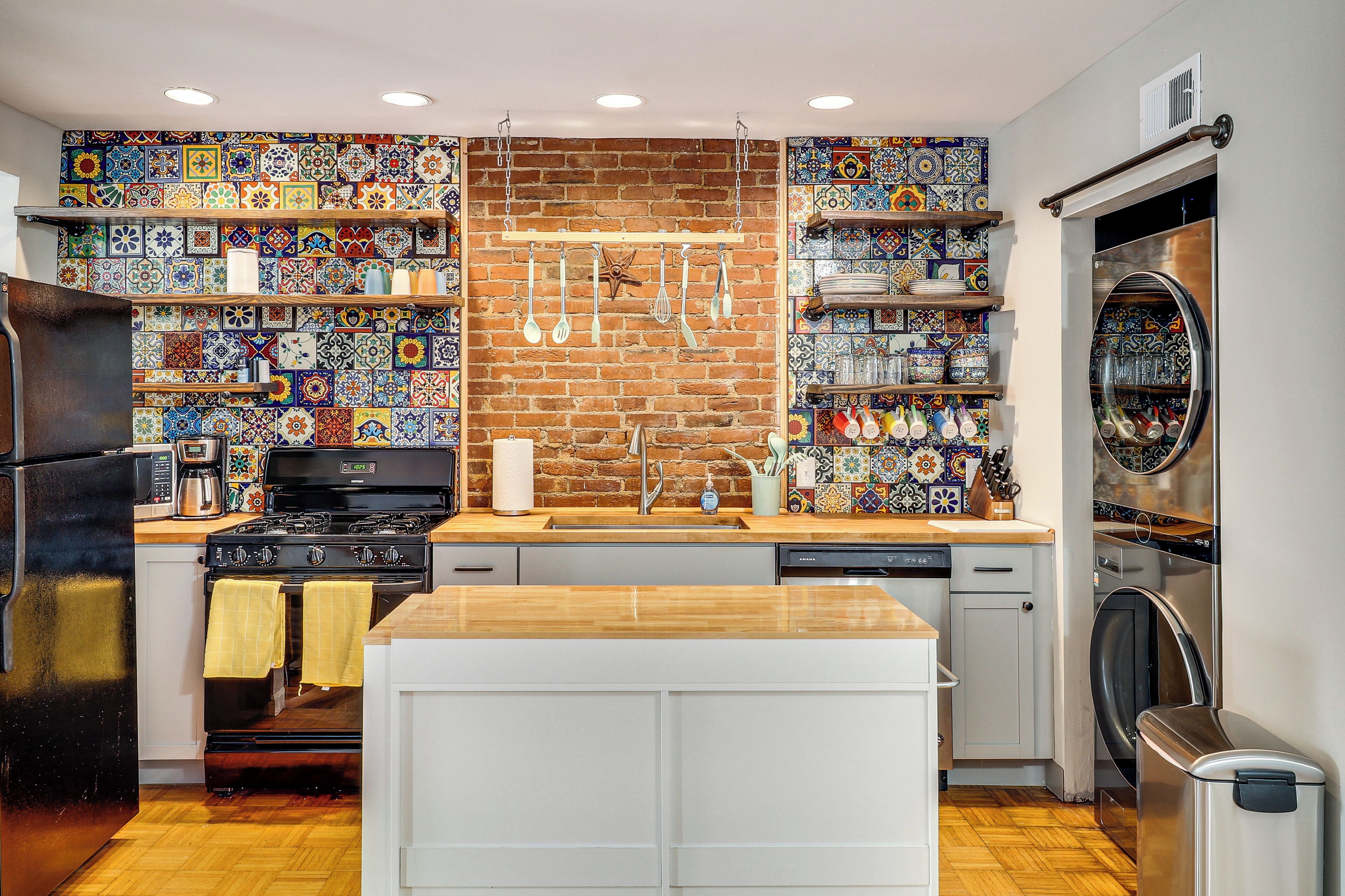 A kitchen with a brick wall, wooden countertops, a central island, and a stainless steel refrigerator.