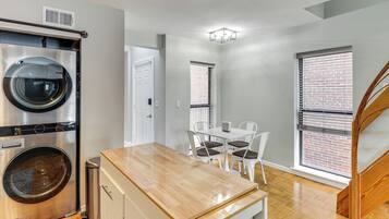 A compact kitchen with a built-in washer and dryer, a small dining area with a table and chairs, and a staircase leading to another level.