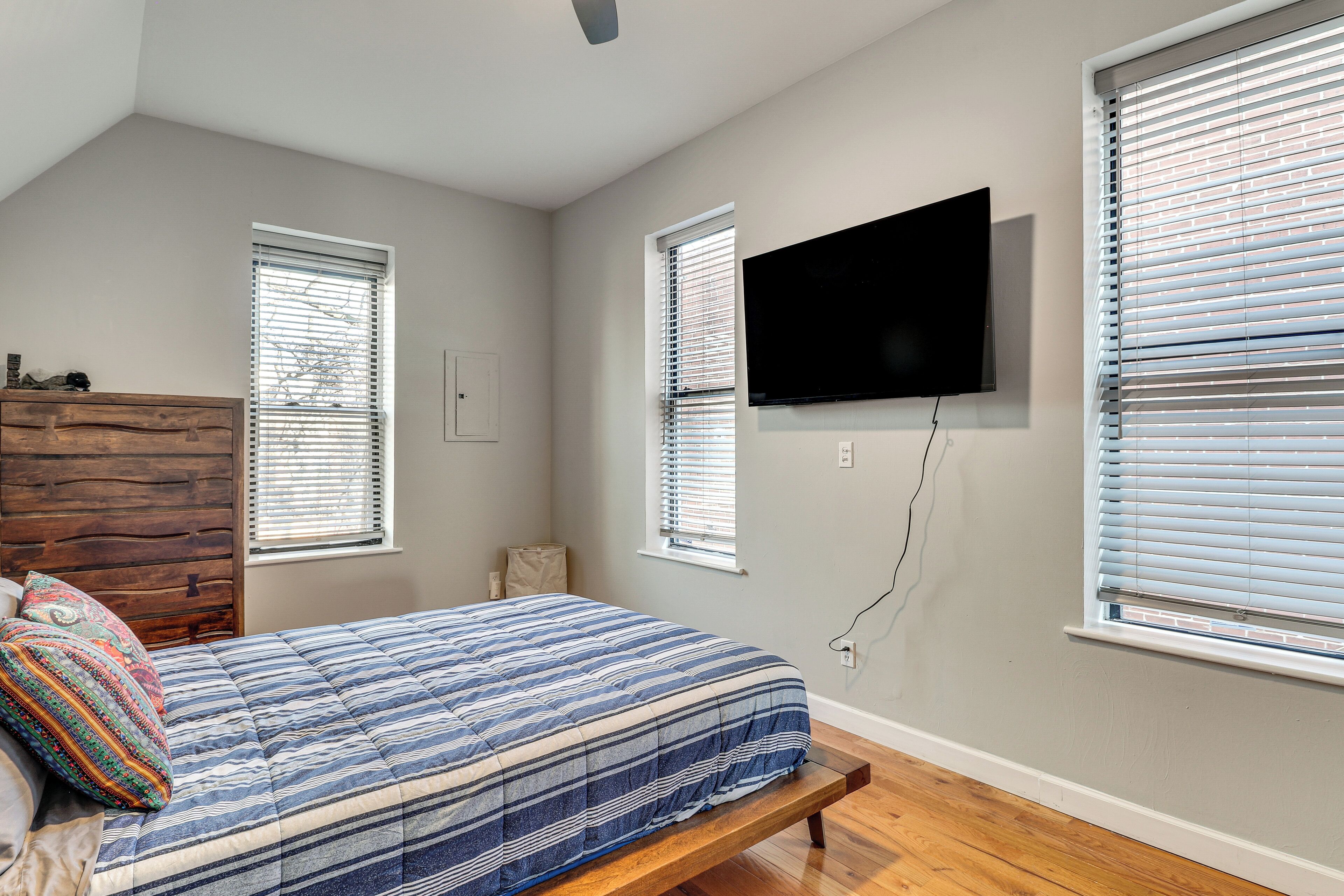 Un dormitorio con cama, cabecero de madera y televisor montado.