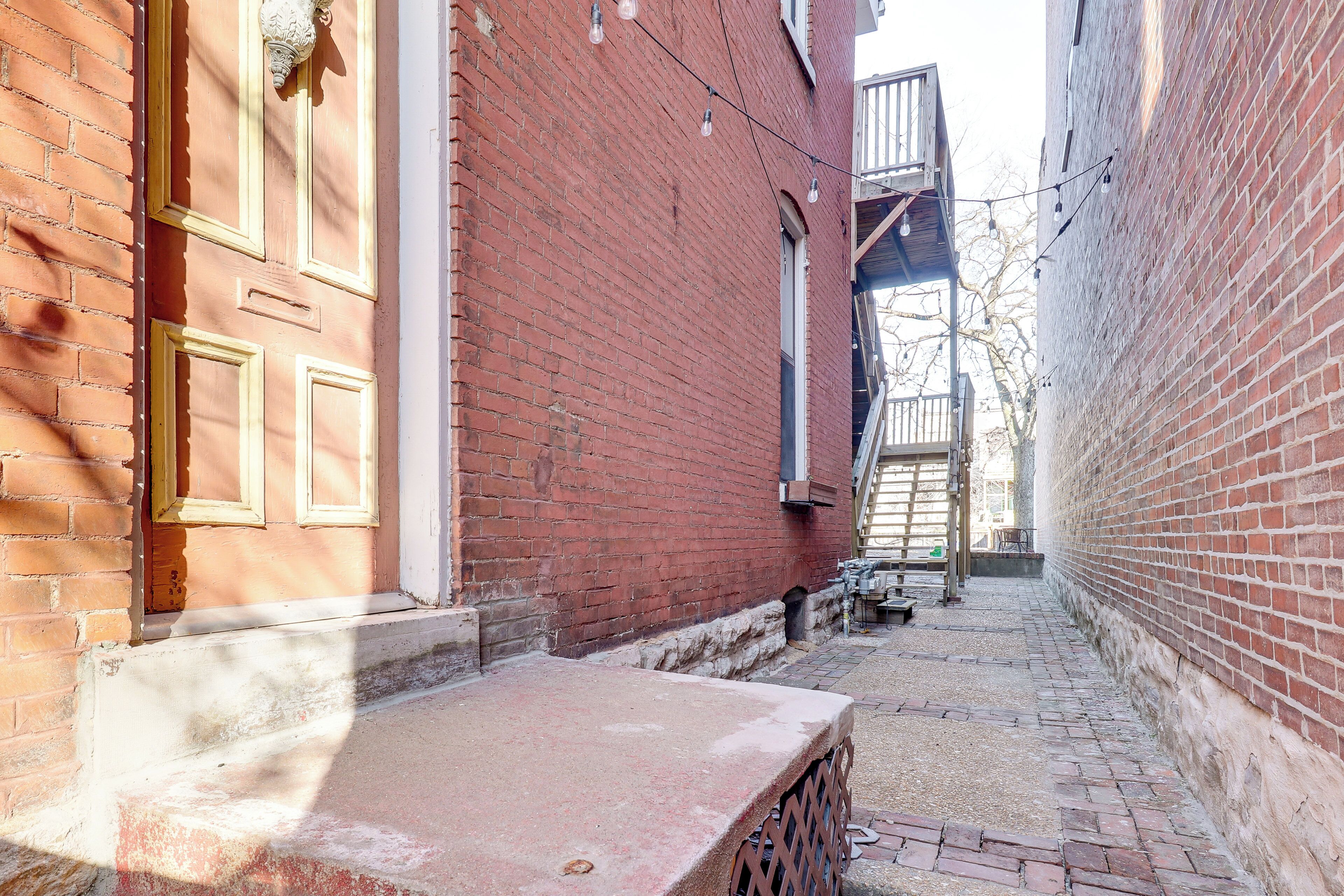 Une ruelle étroite bordée d’immeubles en briques rouges, avec un banc en bois et une petite table.