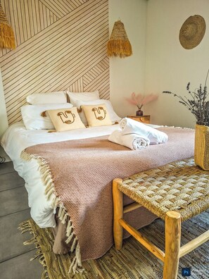 A neatly made bed with a patterned bedspread, pillows with a unique design, and a woven bench beside it. - Refreshing Vacation Rental with a Private Hot Tub in Douelle – Peace and Nature (Douelle)