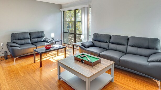 Un salon moderne avec deux canapés gris, une table basse en bois et une table de billard.