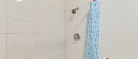 A small, tiled bathroom with a shower, toilet, and a blue shower curtain.