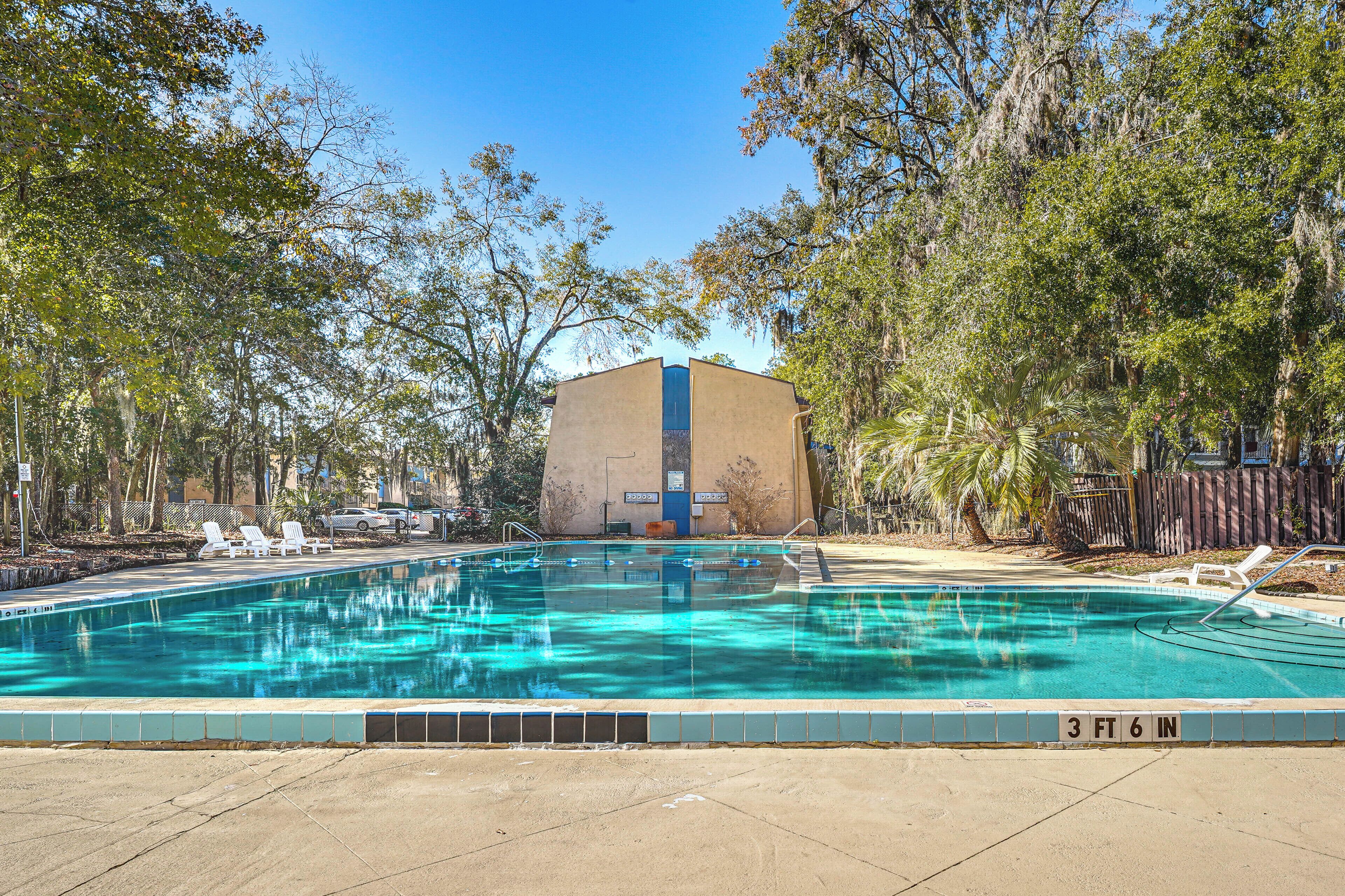 Una piscina con una profundidad de 1 metro 10 centímetros, rodeada de árboles y un edificio con puerta azul.