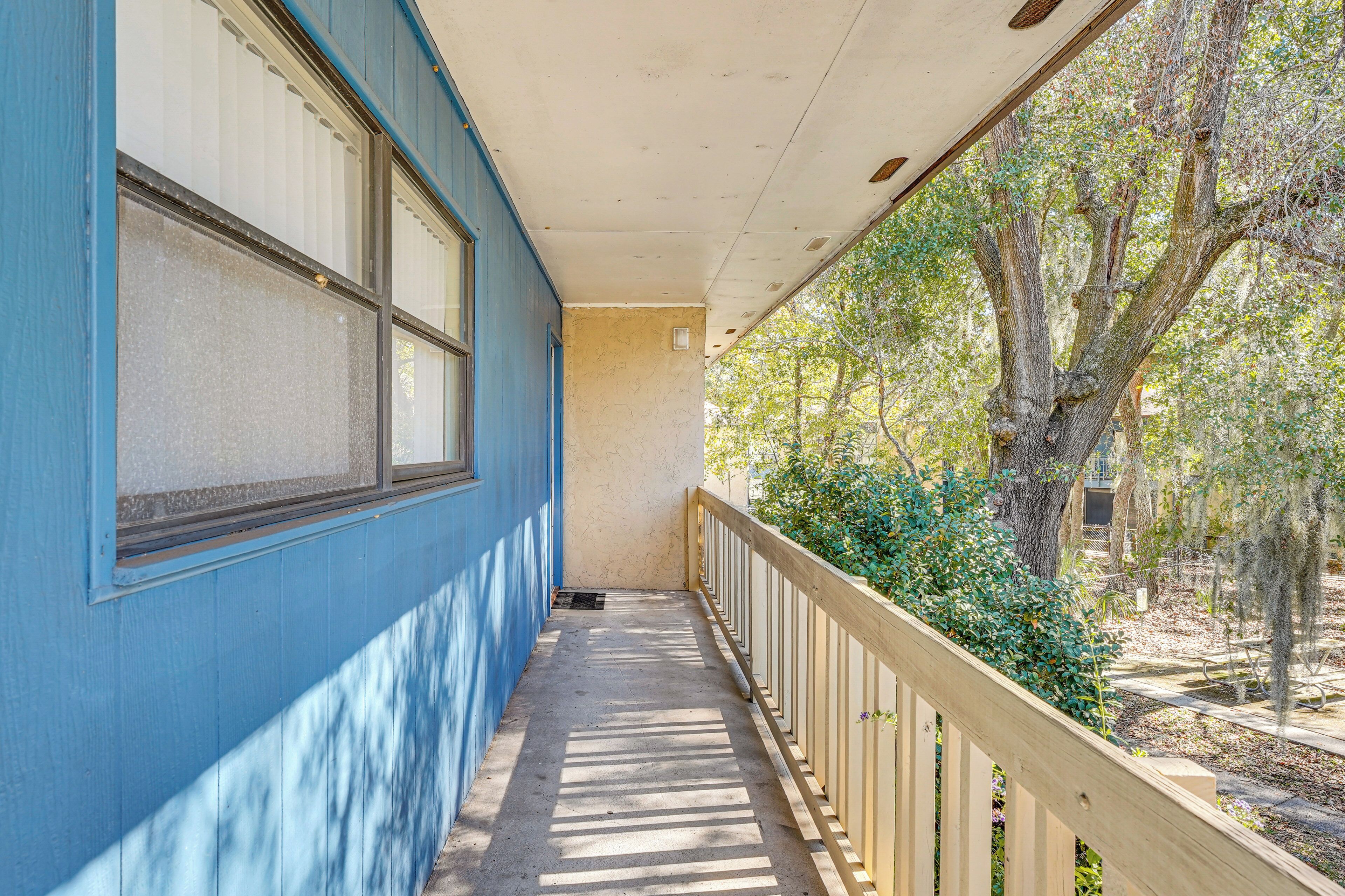 A covered porch with a wooden railing, a blue exterior wall, and a view of trees and greenery.
