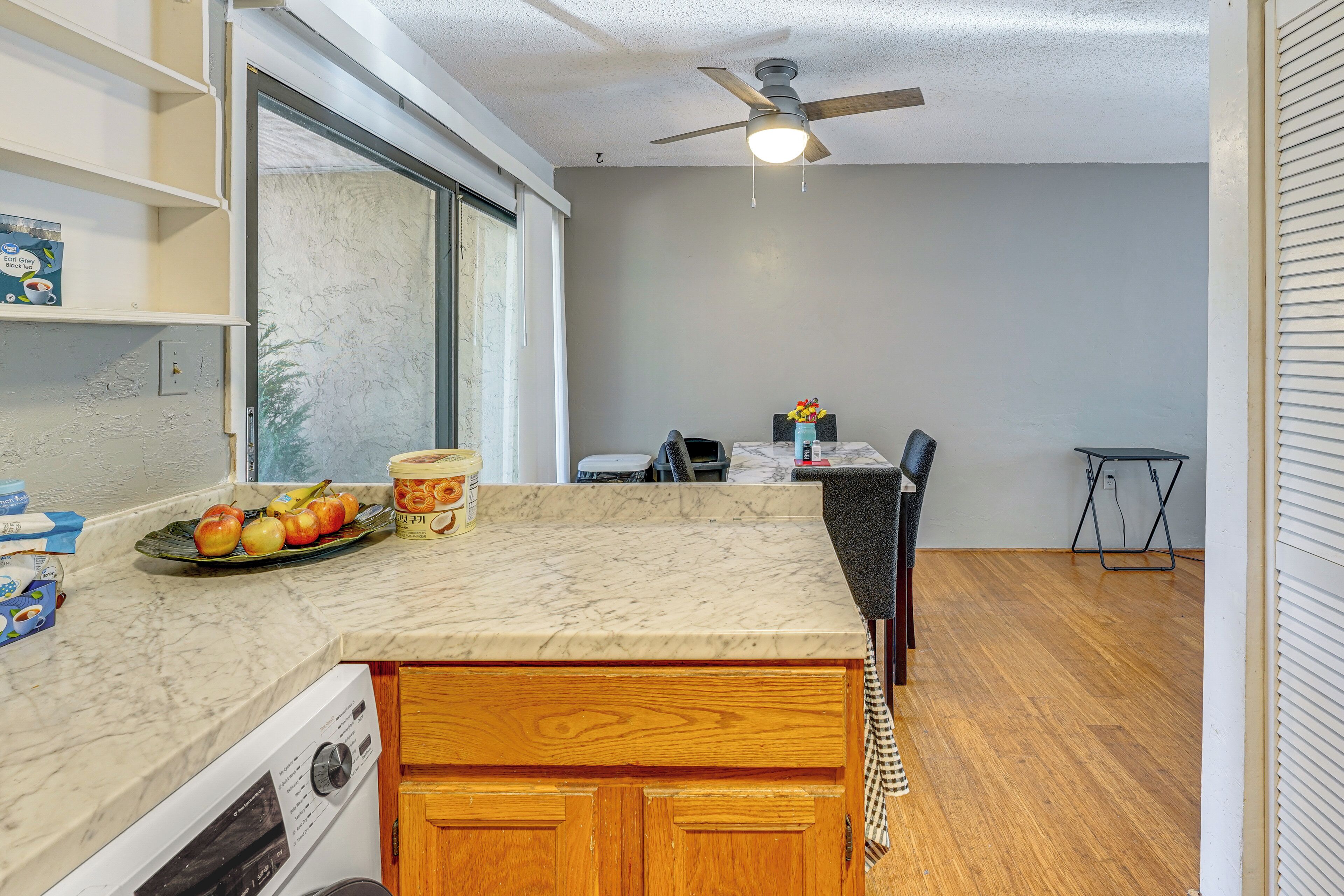 A kitchen with a marble countertop, wooden cabinets, a ceiling fan, and a window with blinds.