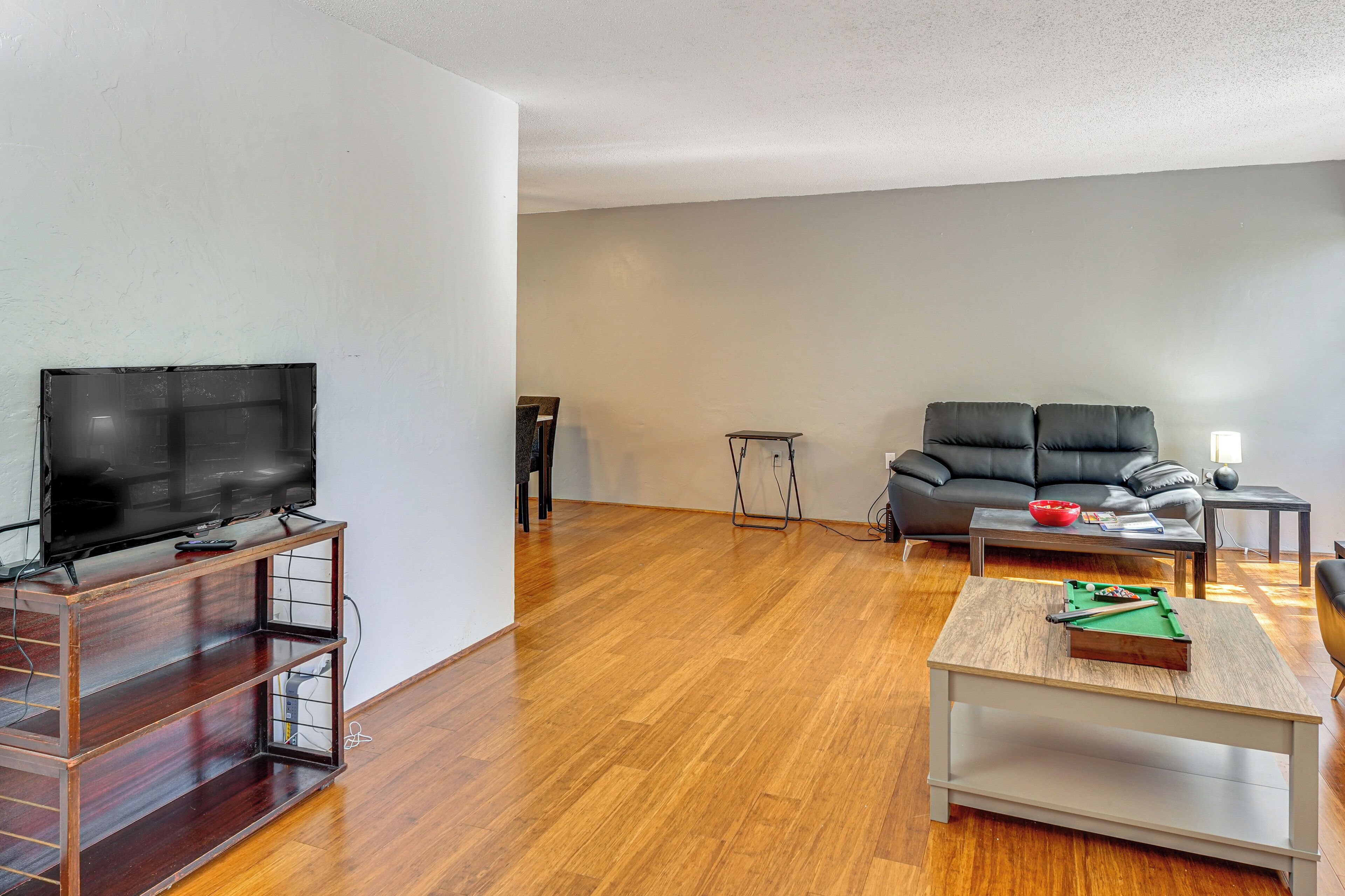 A living room with a TV on a wooden stand, a sofa, a coffee table with a pool table, and a lamp.