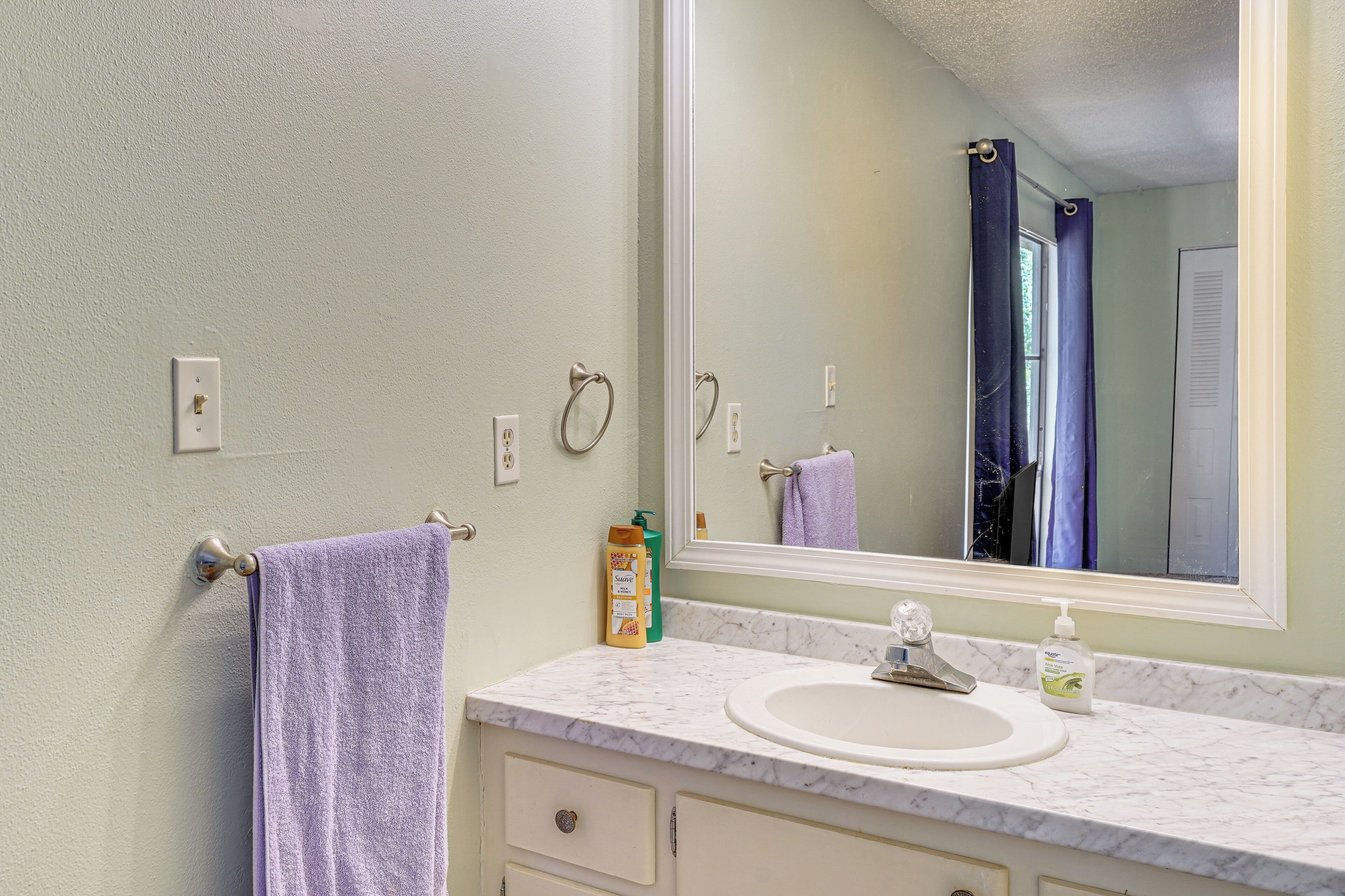 A bathroom with a white marble sink, a large mirror, and a towel hanging on a towel rack.