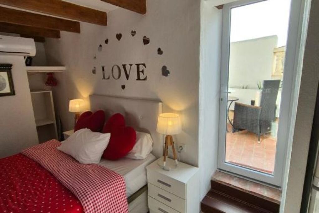 A bedroom with a bed, a wall decoration saying "LOVE", a window, and a view of an outdoor patio.