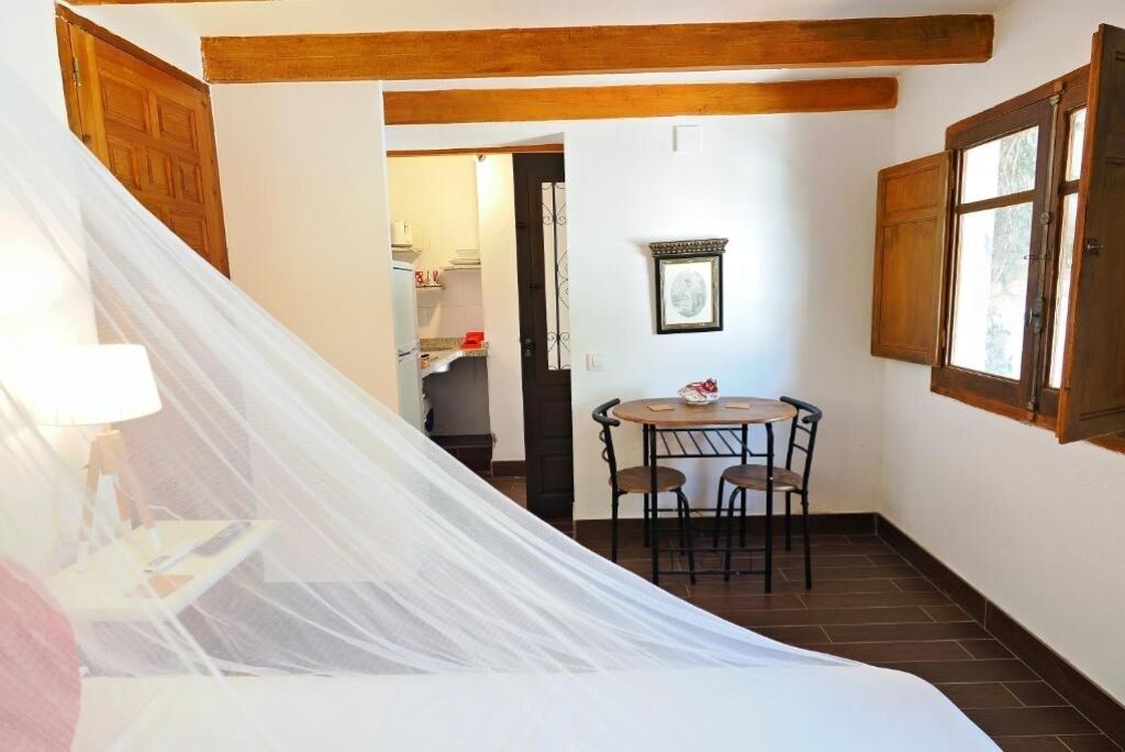 Una habitación con una cama, una mesa y sillas, vigas de madera en el techo y una ventana.