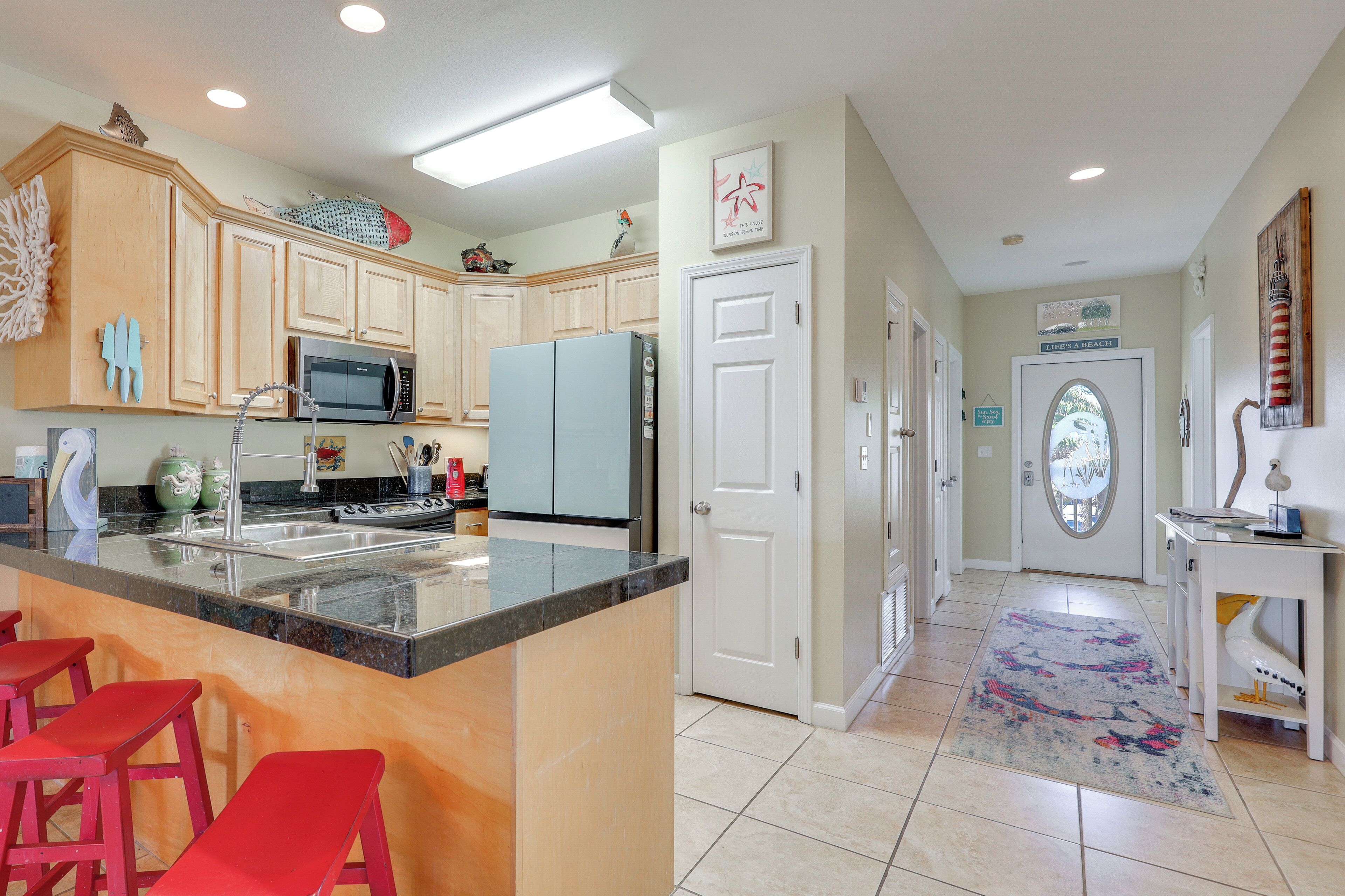 A kitchen with a central island, red bar stools, wooden cabinets, a microwave, and a refrigerator.