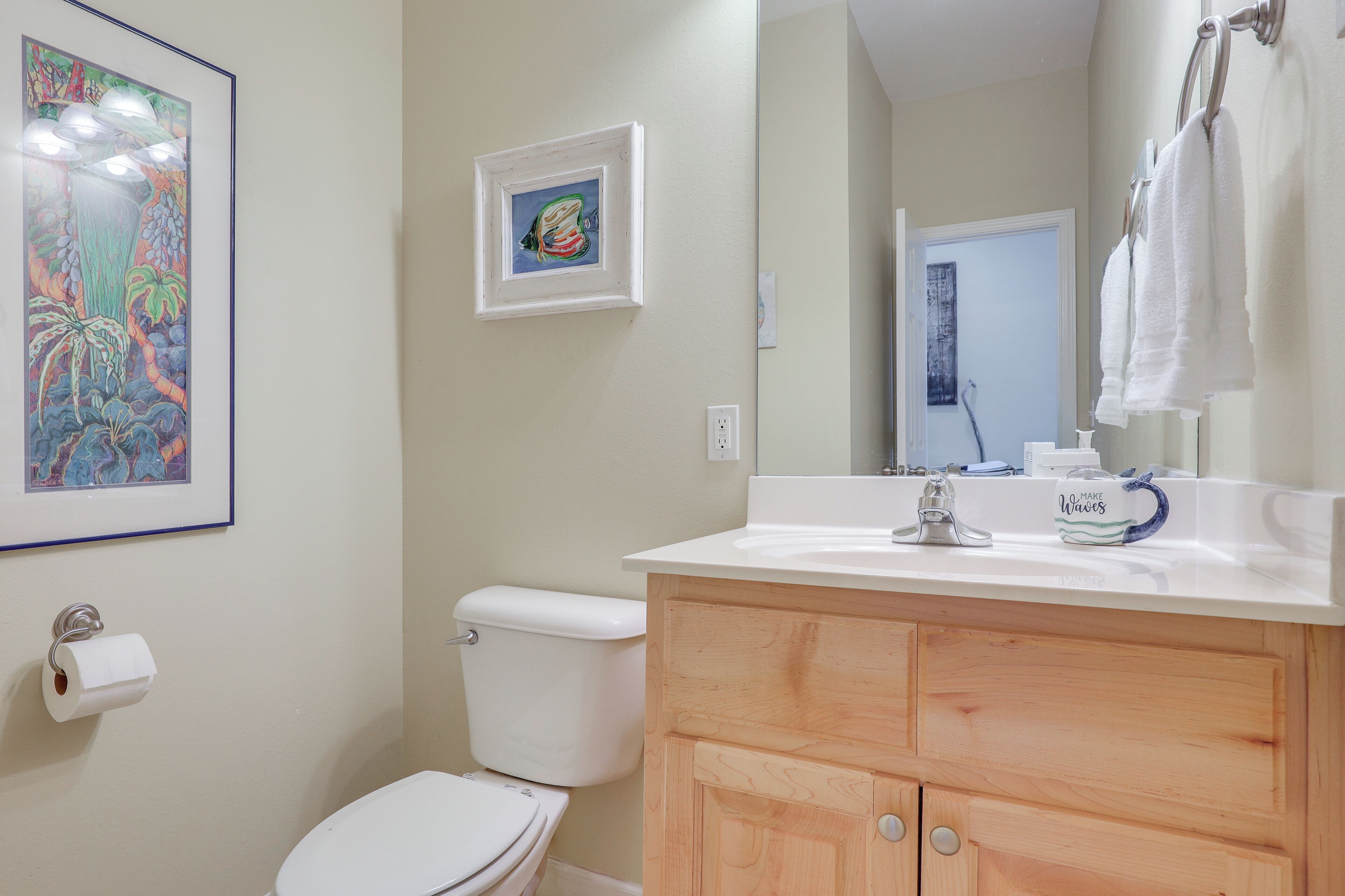 A bathroom with a toilet, a sink, a mirror, and a framed picture on the wall.
