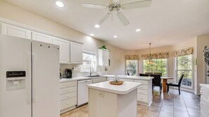 A modern kitchen with white cabinetry, a central island, and a dining area with a table and chairs. - 2 Mi to Pinehurst Resort: Spacious Golf Getaway! (Pinehurst)