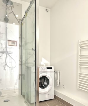 A modern bathroom with a glass-enclosed shower, a built-in washing machine, and a towel rack. - Superb T2 facing Tête d'Or and Cité internationale (Caluire-et-Cuire)