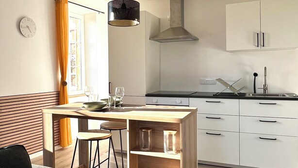 Una cocina moderna con una isla de madera, armarios blancos y una lámpara colgante negra.