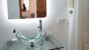 Et badeværelse med en vask af glas, et spejl og en trædør.