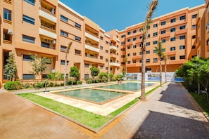 A multi-story hotel with a swimming pool, outdoor seating, and palm trees. - New Appart à Guéliz, piscine, balcon et parking (Marrakesh)