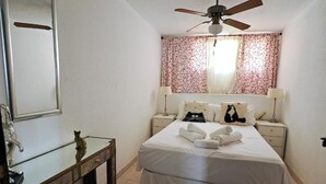 Une chambre à coucher comprenant un lit, un ventilateur de plafond, une table de chevet, un miroir et un objet décoratif posé sur la commode.