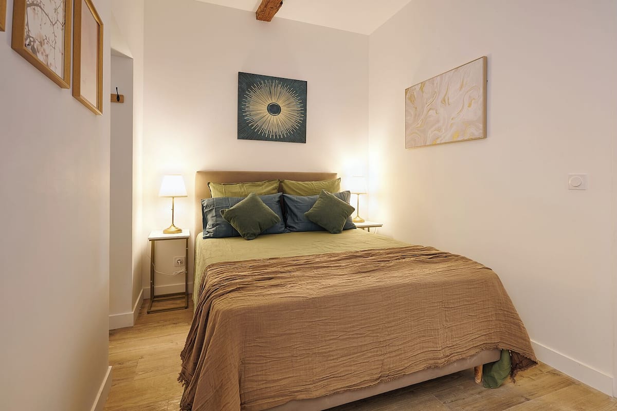 A bedroom with a bed, bedside lamps, and artwork on the walls.
