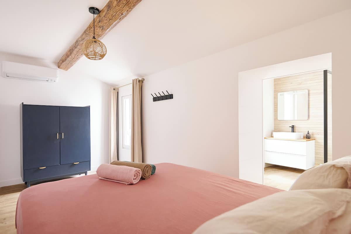 A bedroom with a bed, a wardrobe, a bathroom with a mirror, and a hanging light fixture.